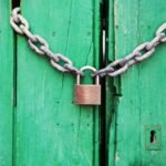 A rustic green wooden door secured with a heavy chain and padlock, symbolizing security.