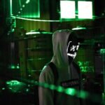 Man in a hoodie with glowing mask amidst neon green lights, evoking mystery and intrigue.