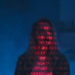 A mysterious silhouette with red binary code projected over the face, set against a dark, moody background.